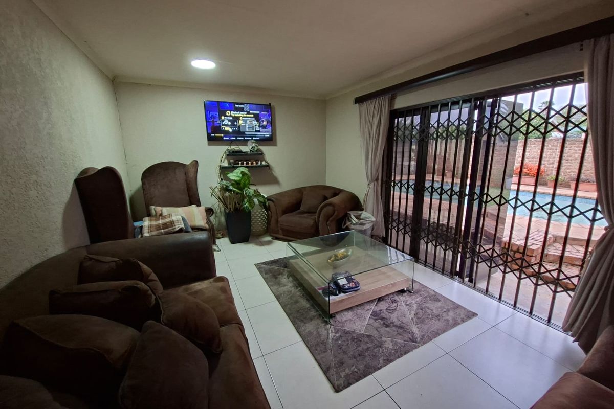 A comfortable living room featuring tiled flooring and large sliding glass doors with security gates, providing direct access to the outdoor pool area.