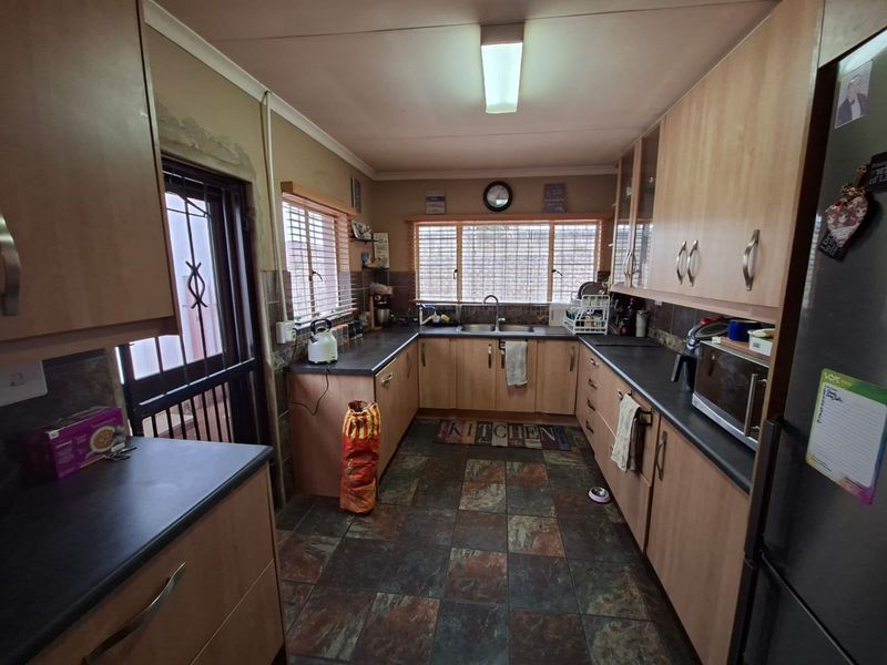 Functional kitchen featuring laminate cabinetry, dark countertops, double sink, and tiled flooring with direct access to the exterior via a security gate.