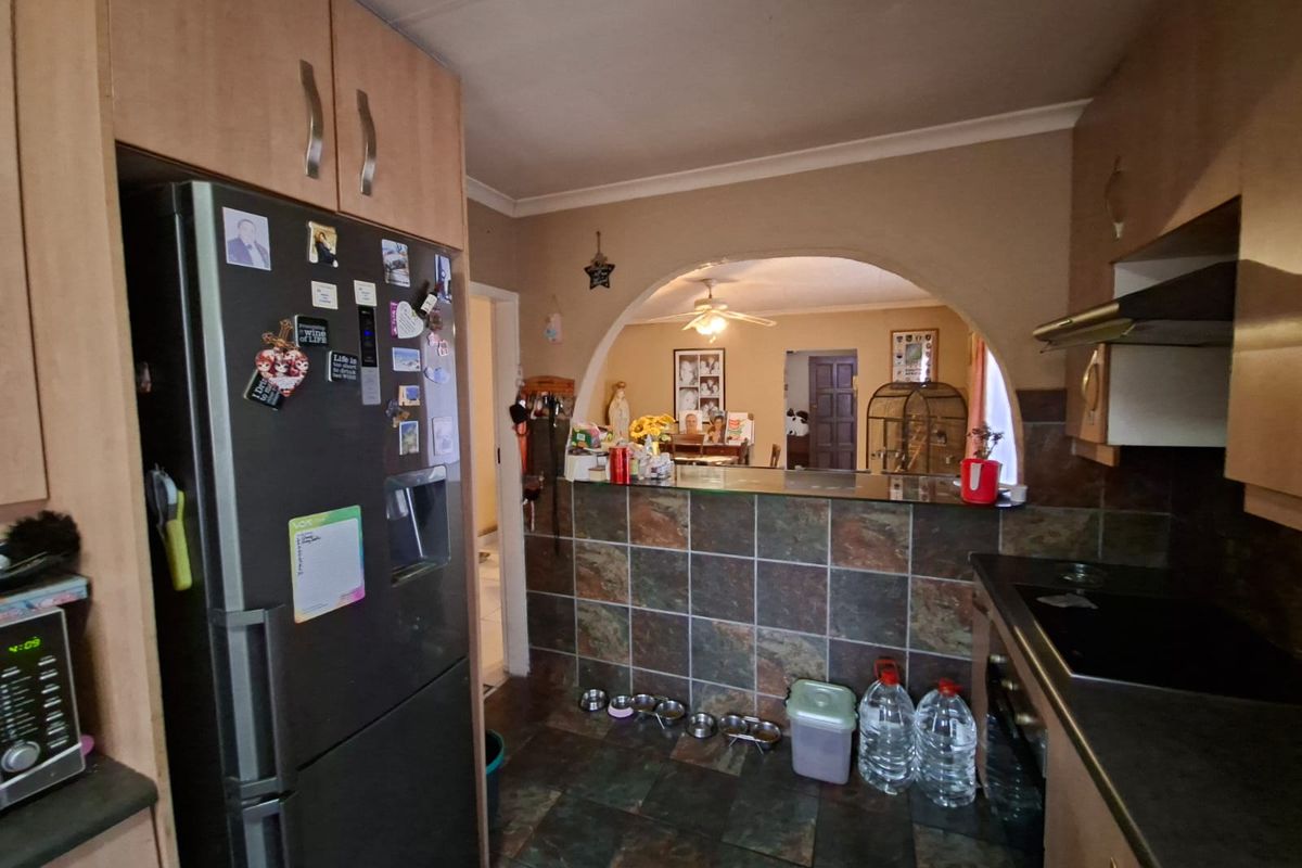 A functional kitchen featuring tiled flooring, a breakfast bar with a tiled facade, and an arched opening leading to the adjacent living area.