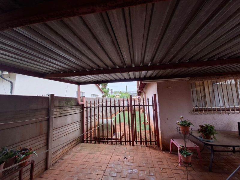 A covered outdoor patio area featuring paved flooring, a corrugated metal roof, and a secure metal gate leading to the rear garden.