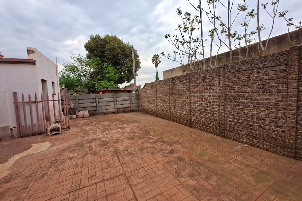 A spacious rear courtyard featuring paved flooring and enclosed by high precast and brick boundary walls with a metal security gate.