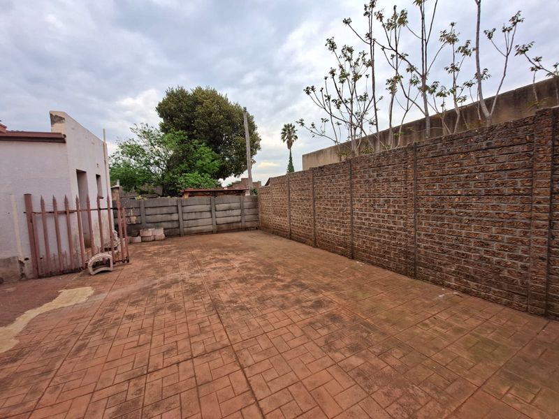 A spacious rear courtyard featuring paved flooring and enclosed by high precast and brick boundary walls with a metal security gate.