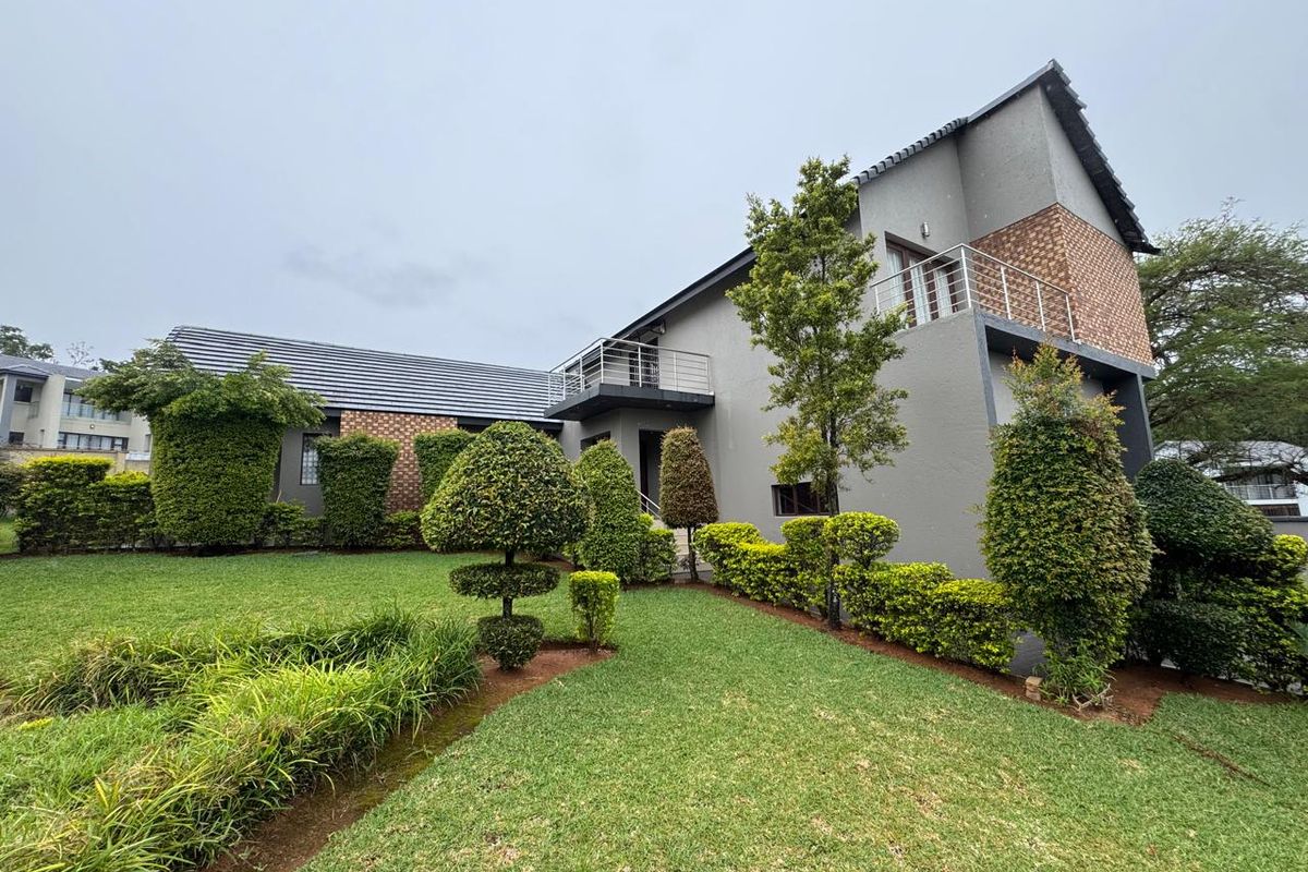 A well-maintained two-story house exterior featuring a landscaped garden, brick accents, and a private balcony with metal railings.