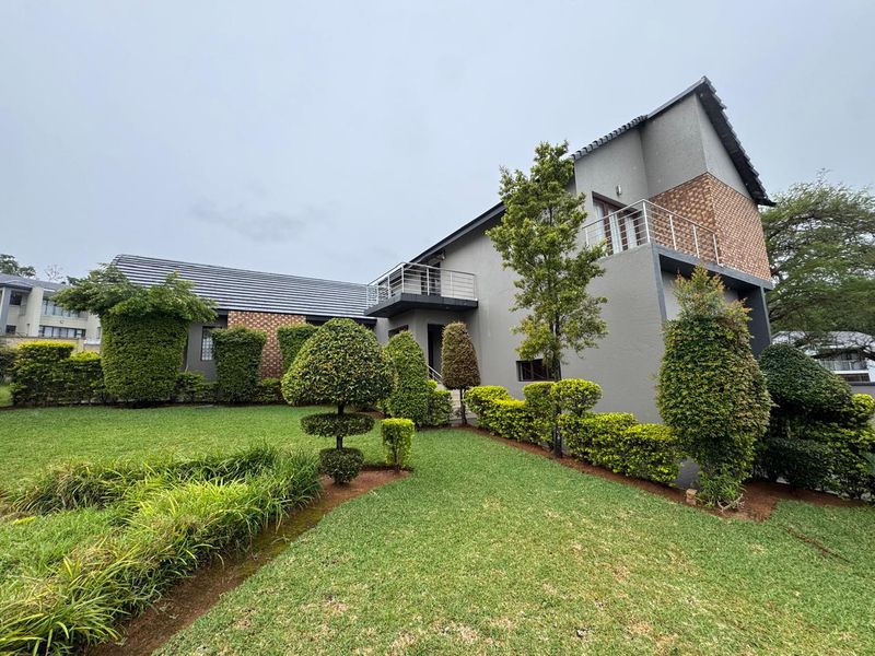 A well-maintained two-story house exterior featuring a landscaped garden, brick accents, and a private balcony with metal railings.