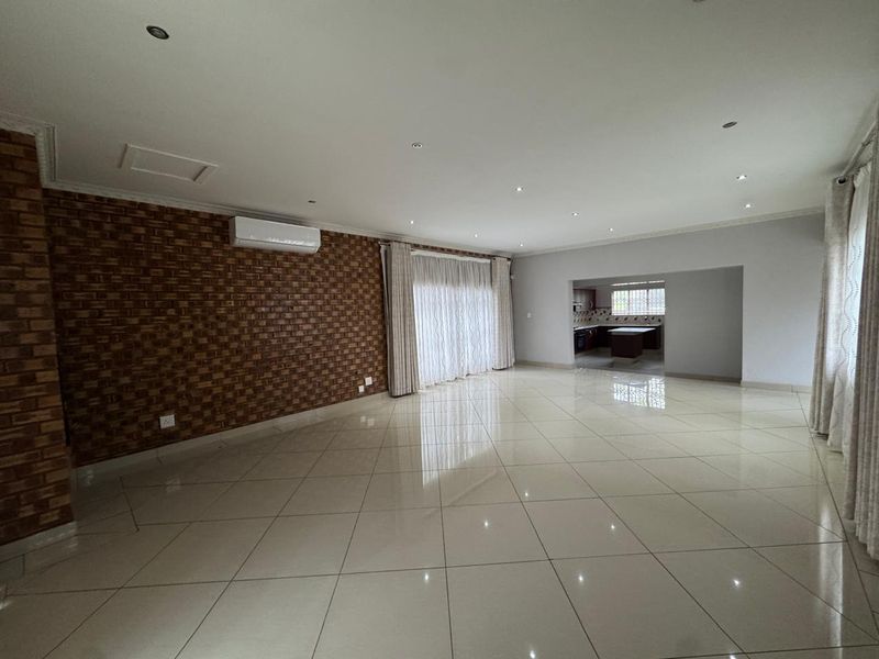 Spacious open-plan living area featuring a brick accent wall, tiled flooring, recessed lighting, and a split-system air conditioner, with a view into the kitchen.