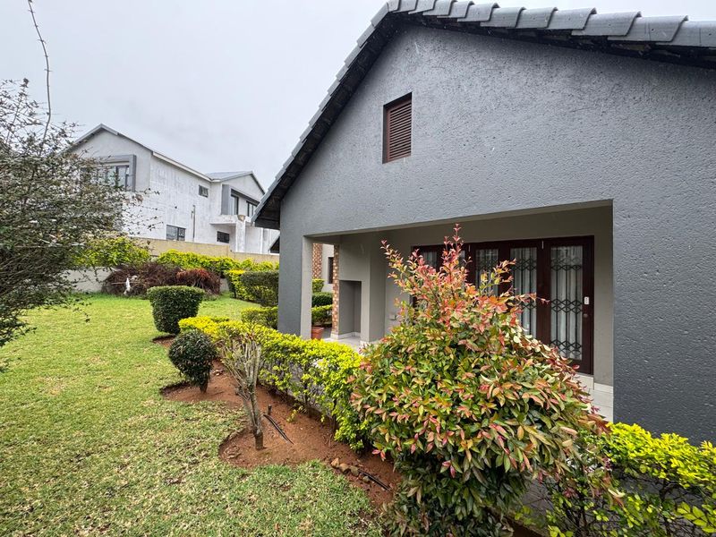A view of the rear exterior featuring a covered patio, landscaped garden, and a modern grey textured facade with a tiled roof.
