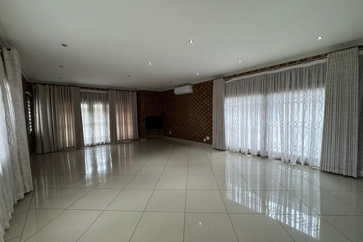 Spacious, light-filled living area featuring large porcelain floor tiles, recessed downlighting, split-system air conditioning, and expansive sliding glass doors with floor-to-ceiling curtains.