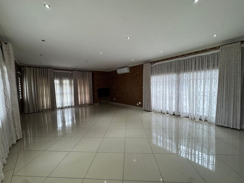 Spacious, light-filled living area featuring large porcelain floor tiles, recessed downlighting, split-system air conditioning, and expansive sliding glass doors with floor-to-ceiling curtains.