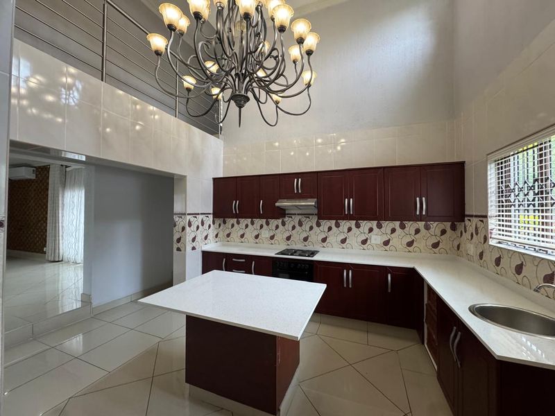 Spacious kitchen featuring dark wood cabinetry, stone countertops, a central island, and a double-volume ceiling with a feature chandelier.