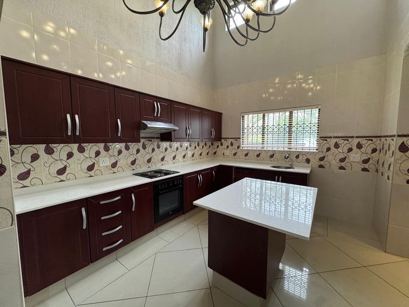 Spacious kitchen featuring dark wood cabinetry, stone countertops, a central island, built-in oven and hob, and high ceilings with a decorative chandelier.