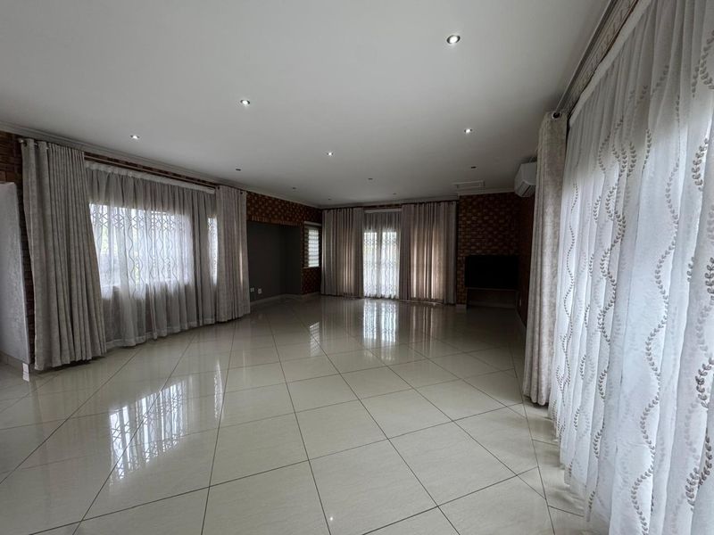 Spacious, light-filled living area featuring polished porcelain tiles, exposed brick accents, recessed lighting, and split-system air conditioning.