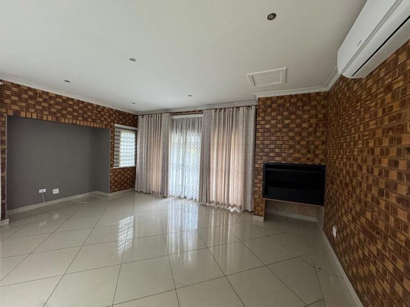 Spacious living room featuring exposed brick walls, tiled flooring, a built-in fireplace, and a wall-mounted air conditioning unit with access to the outdoors.