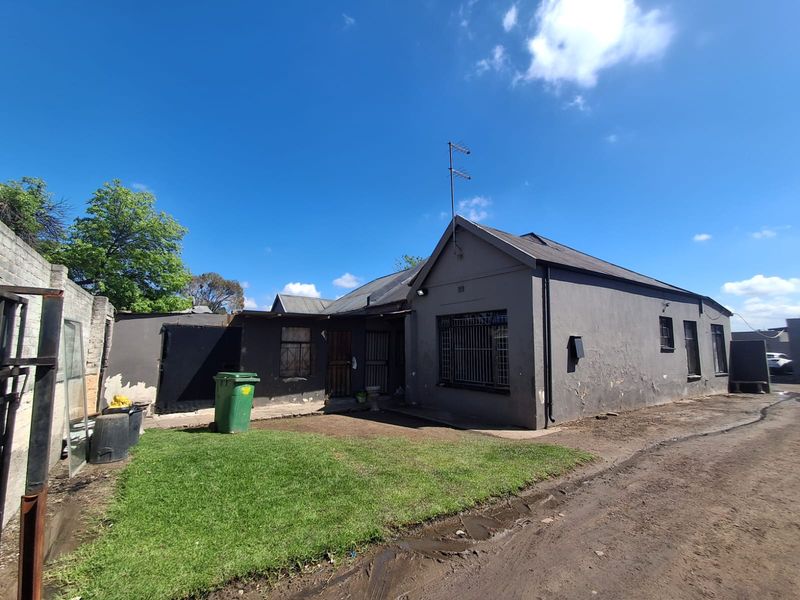 Rear view of a detached house featuring a small lawn, security bars on windows, and a pitched roof, showing signs of exterior maintenance requirements.