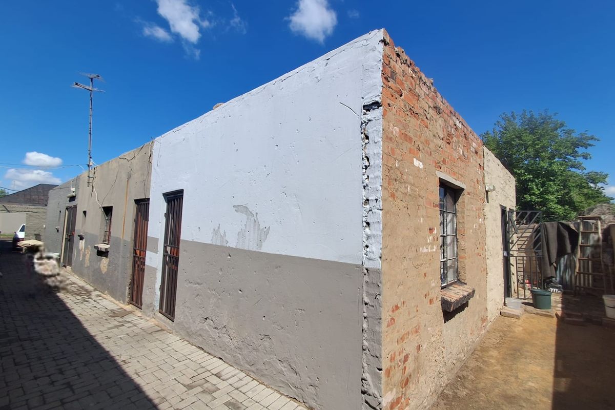 Rear exterior view of the property showing exposed brickwork, security gates, and paved walkway, requiring significant maintenance and exterior restoration.