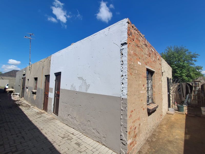 Rear exterior view of the property showing exposed brickwork, security gates, and paved walkway, requiring significant maintenance and exterior restoration.