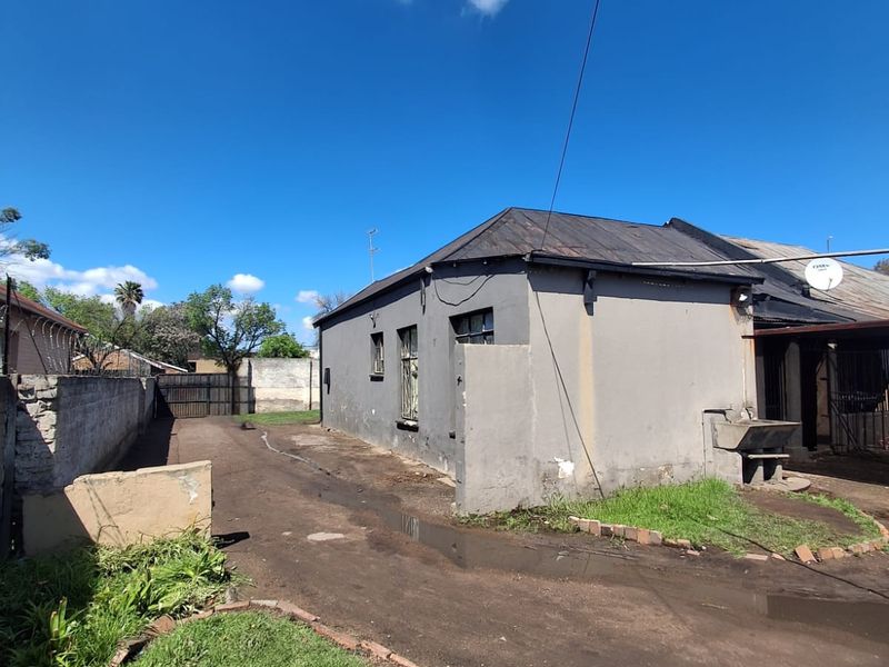 Rear exterior view of the property featuring a concrete boundary wall, metal roofing, and an external wash basin area with unpaved ground.
