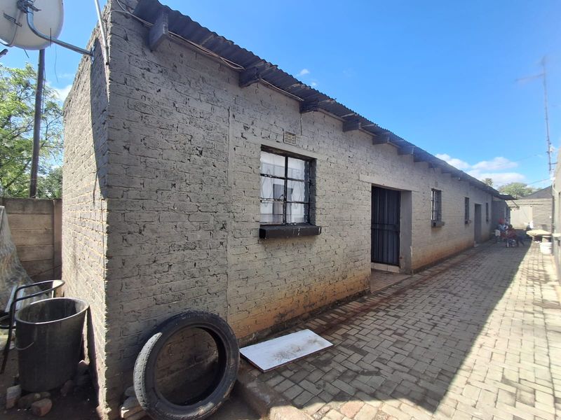 Exterior view of a single-story brick structure with a corrugated metal roof and paved walkway, showing signs of wear and weathering.