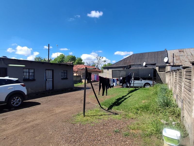 Rear exterior view of the property featuring a dirt driveway, precast concrete boundary wall, and metal roof structures.