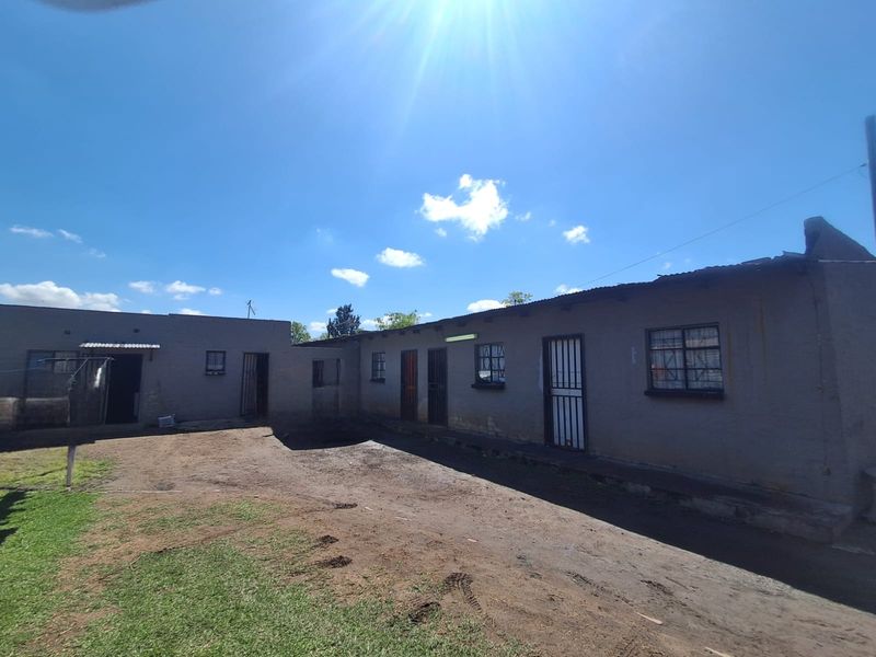 Rear exterior view of the property featuring multiple access points with security gates and steel-framed windows under a corrugated metal roof.