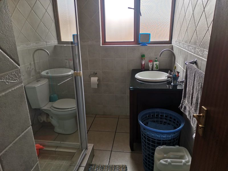 A compact bathroom featuring a vanity with a drop-in basin, a toilet, and a glass-enclosed shower, finished with neutral ceramic wall and floor tiles.