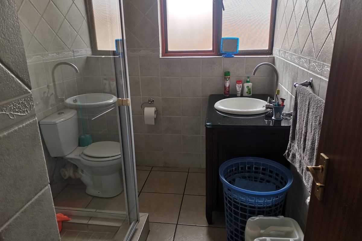 A compact bathroom featuring a vanity with a drop-in basin, a toilet, and a glass-enclosed shower, finished with neutral ceramic wall and floor tiles.