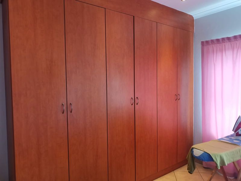 A bedroom featuring extensive floor-to-ceiling built-in wooden cupboards providing ample storage space.