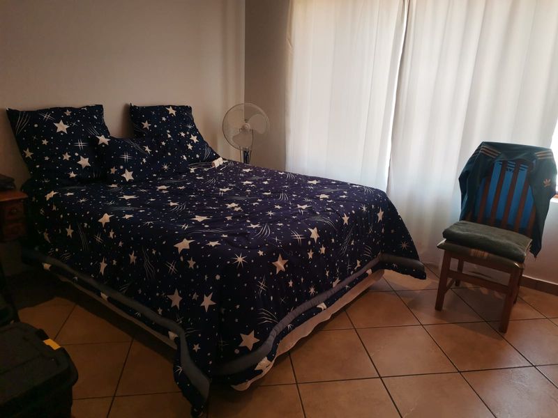 A bedroom featuring tiled flooring and natural light through window curtains.