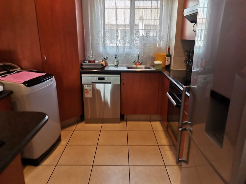 A functional kitchen featuring wood-finish cabinetry, dark countertops, tiled flooring, and integrated appliances including an oven and dishwasher.