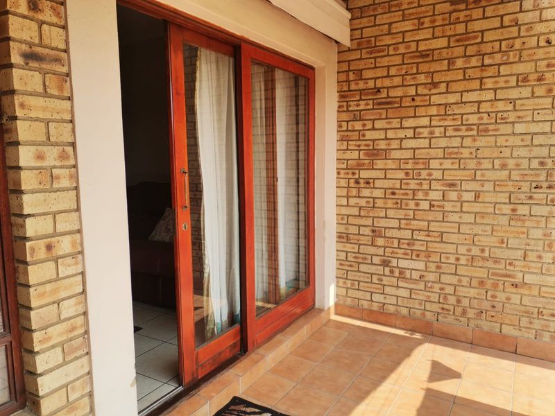 A covered patio area featuring exposed brick walls, tiled flooring, and a wooden-framed sliding glass door leading into the interior.
