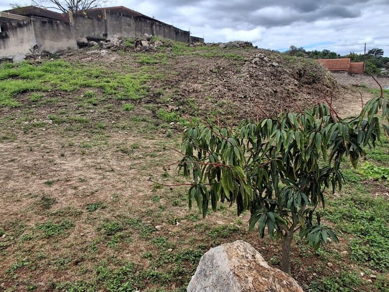 A view of the vacant residential land showing uneven terrain, rocky ground, and surrounding boundary walls.