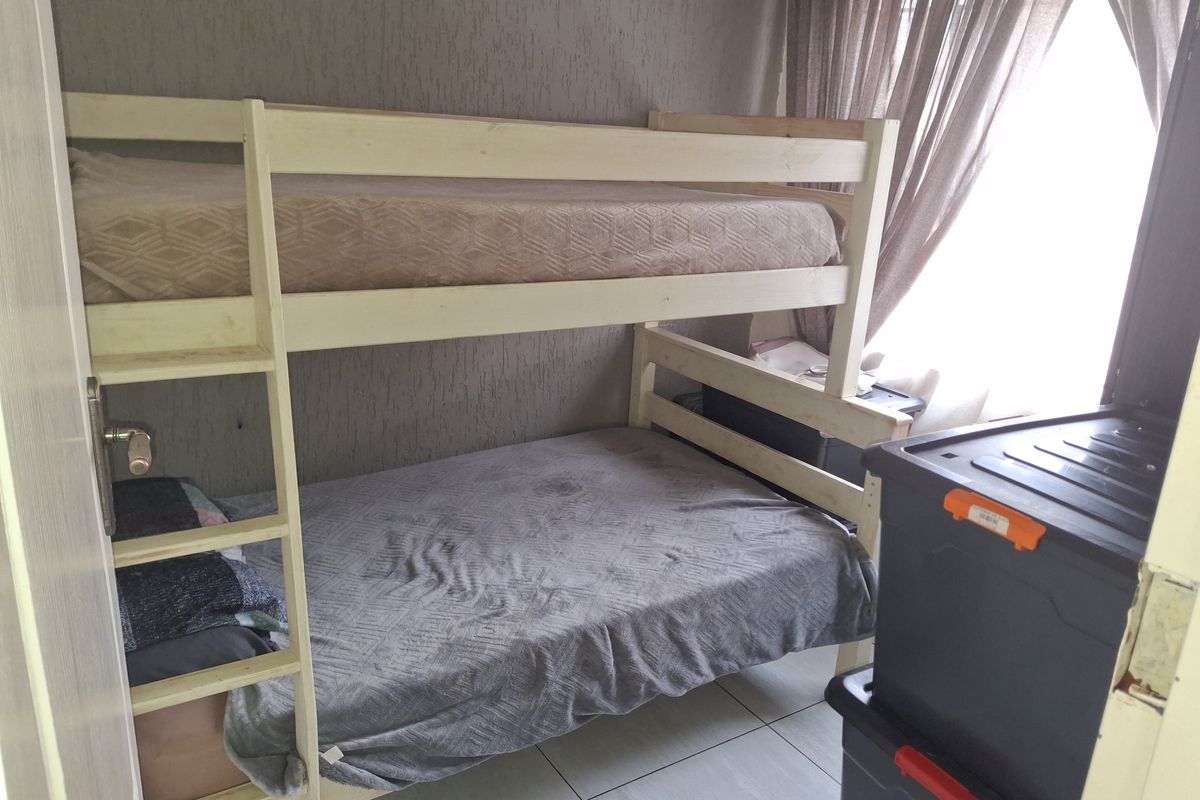 A bedroom featuring tiled flooring and textured wallpaper, providing a functional space for sleeping arrangements.