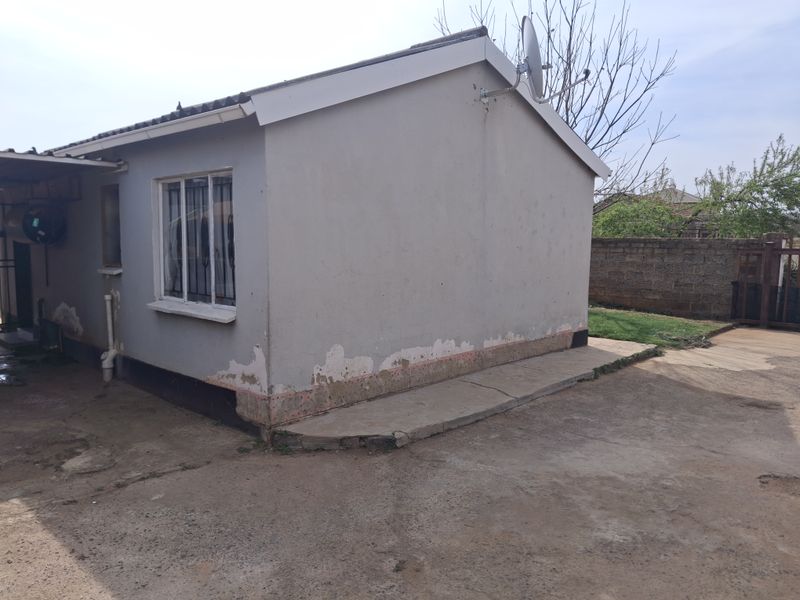 Rear view of the property showing exterior walls with peeling paint and a concrete apron requiring maintenance.