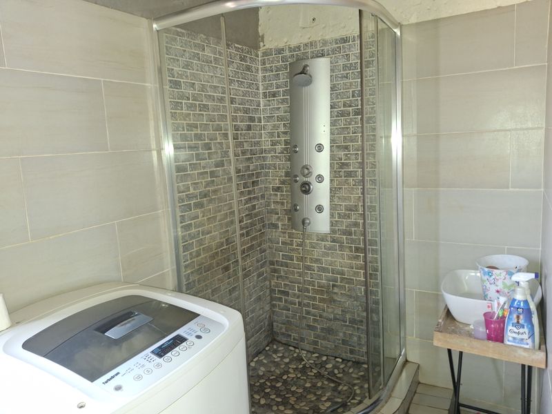 A laundry area featuring a shower enclosure with a modern shower panel, pebble flooring, and wall tiling, requiring some finishing work on the upper walls.