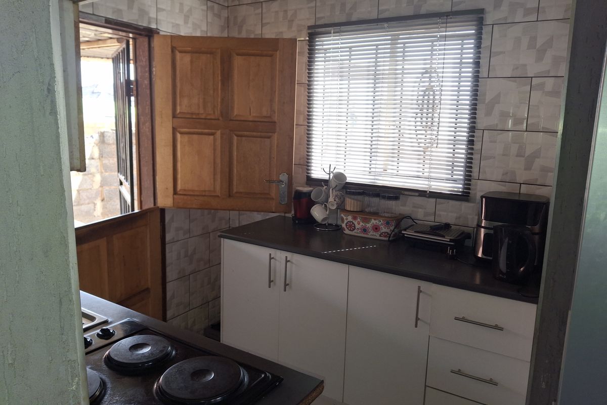 A functional kitchen featuring white cabinetry, dark laminate countertops, an electric hob, and a classic stable door leading to the exterior.