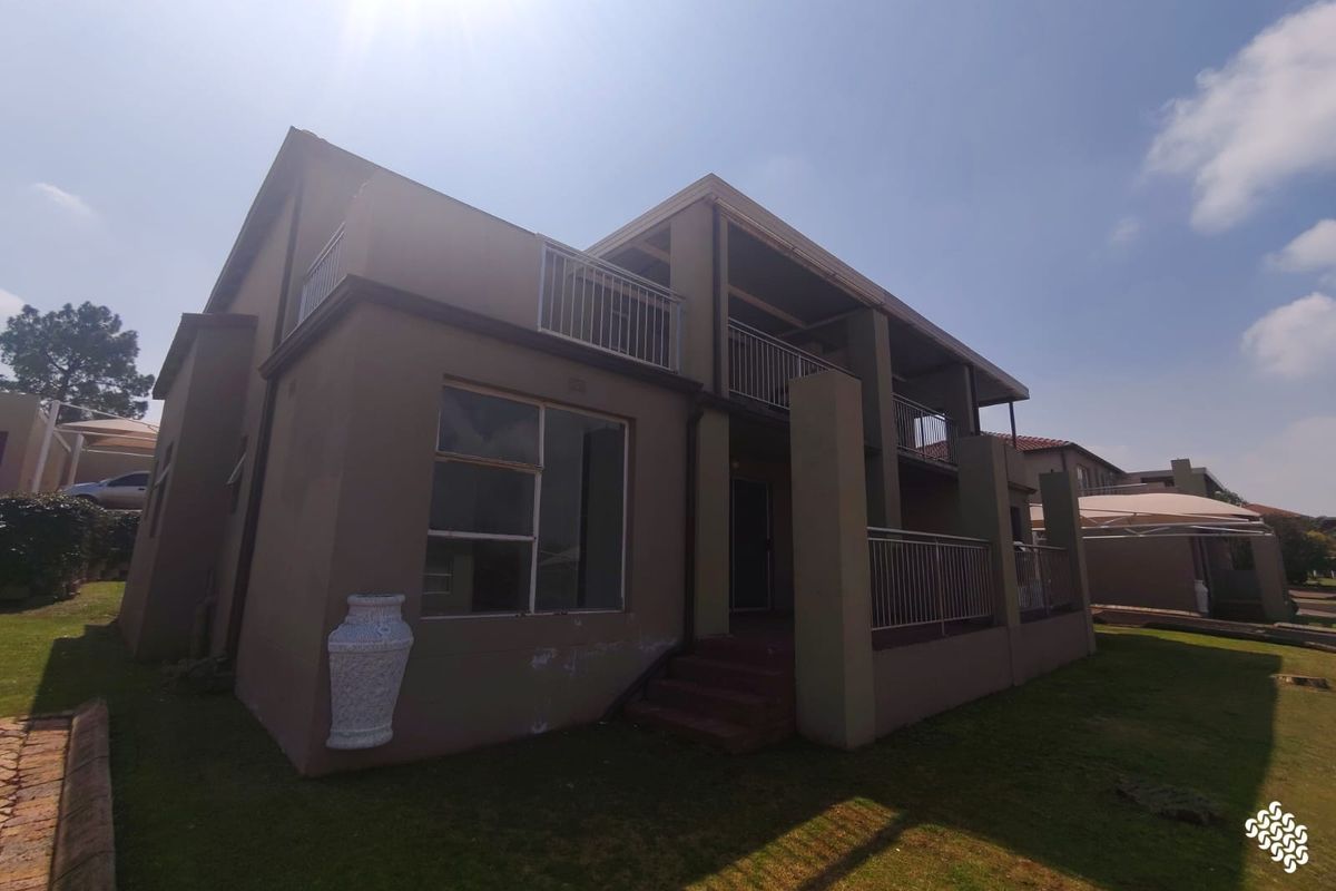 Rear view of a double-story townhouse featuring a balcony with metal railings, sliding doors, and a small lawn area.