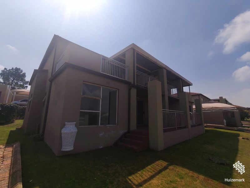 Rear view of a double-story townhouse featuring a balcony with metal railings, sliding doors, and a small lawn area.