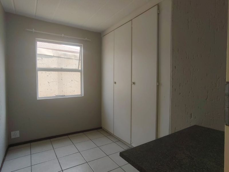 A clean, empty bedroom featuring neutral tiled flooring, built-in cupboards, and a top-hung window providing natural light.