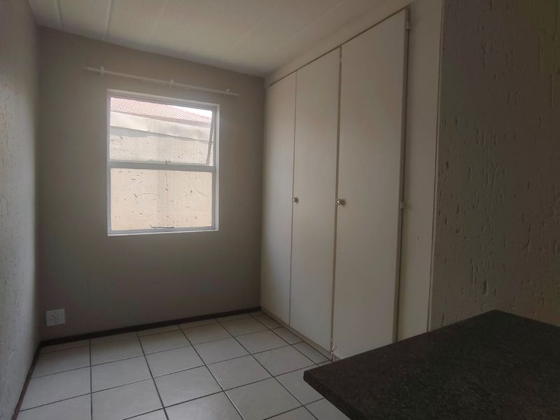 A compact, empty bedroom featuring neutral tiled flooring, built-in cupboards, and a window providing natural light.