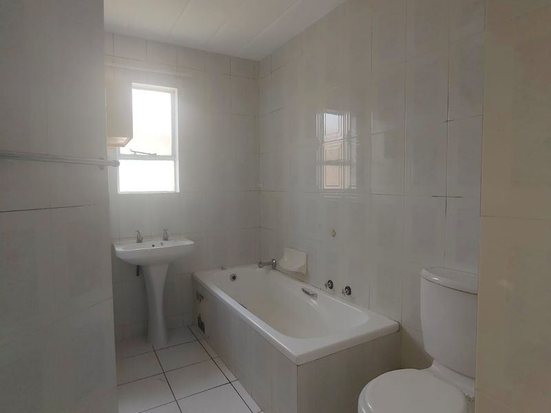 A functional bathroom featuring a pedestal basin, built-in bathtub, and toilet with neutral wall and floor tiling.
