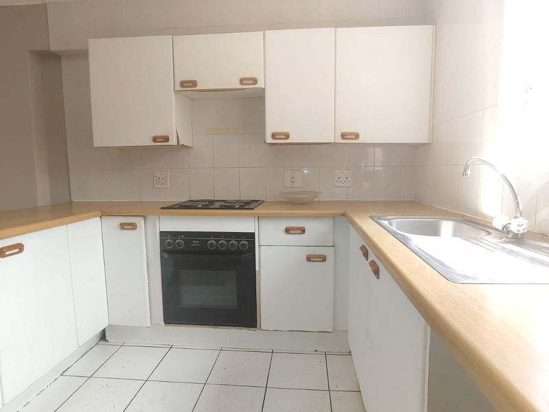 A functional, empty kitchen featuring white cabinetry, laminate countertops, a built-in oven, and tiled flooring, offering a blank canvas for modern updates.