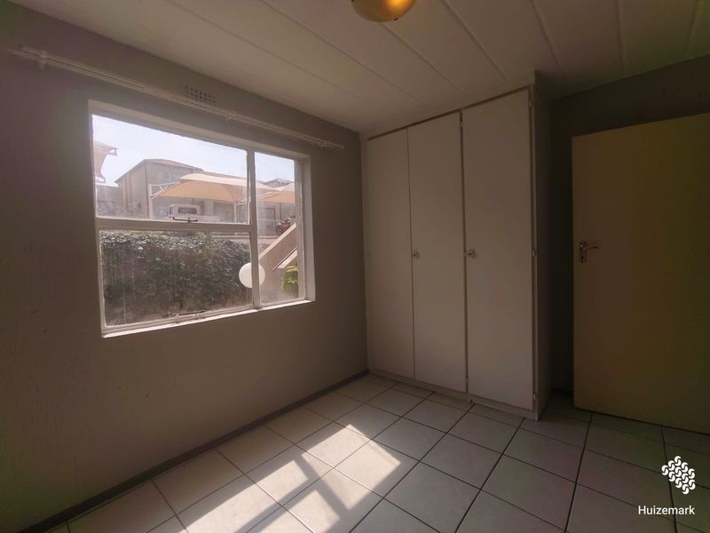 A vacant bedroom featuring tiled flooring, built-in cupboards, and natural light from a large window.