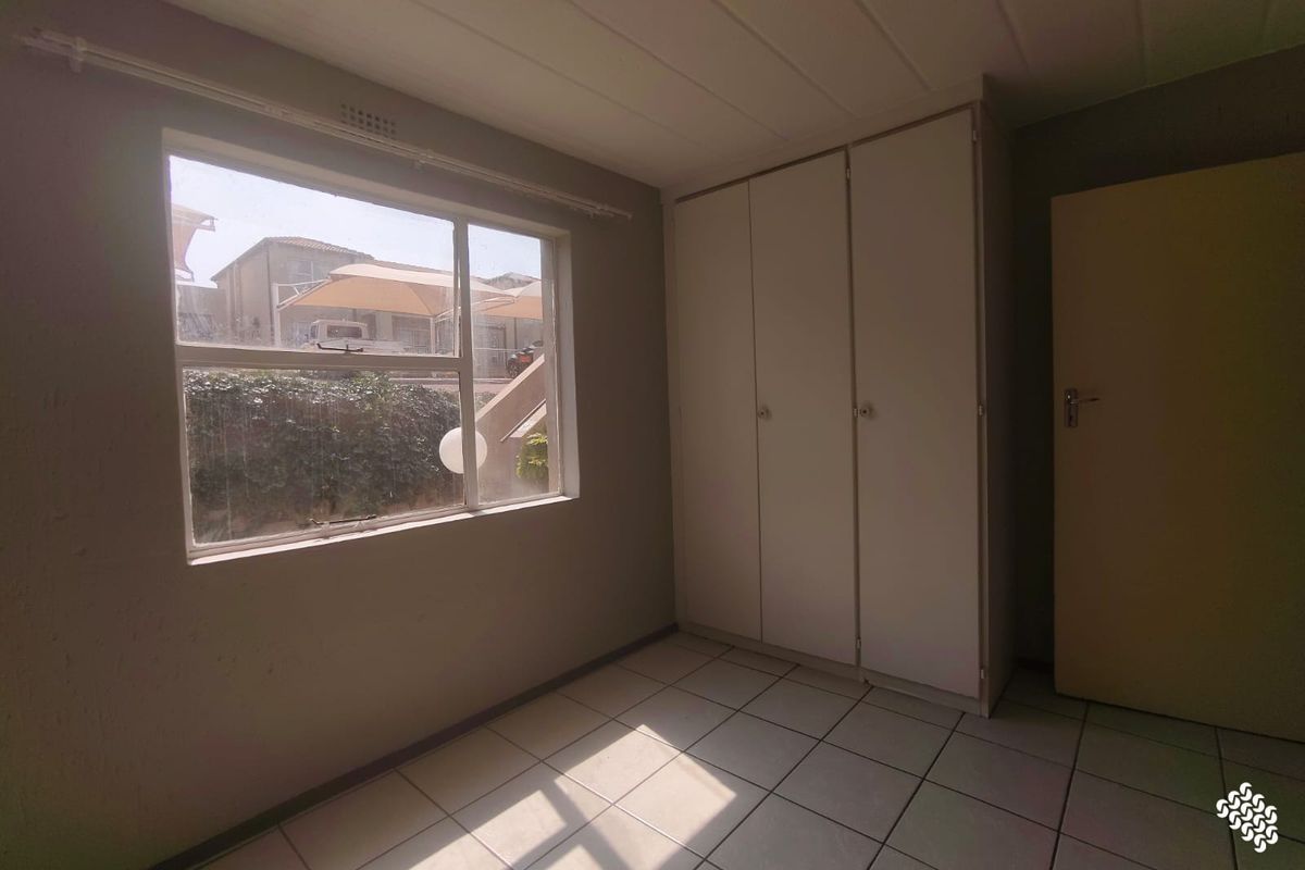A vacant bedroom featuring tiled flooring, built-in cupboards, and natural light from a large window.