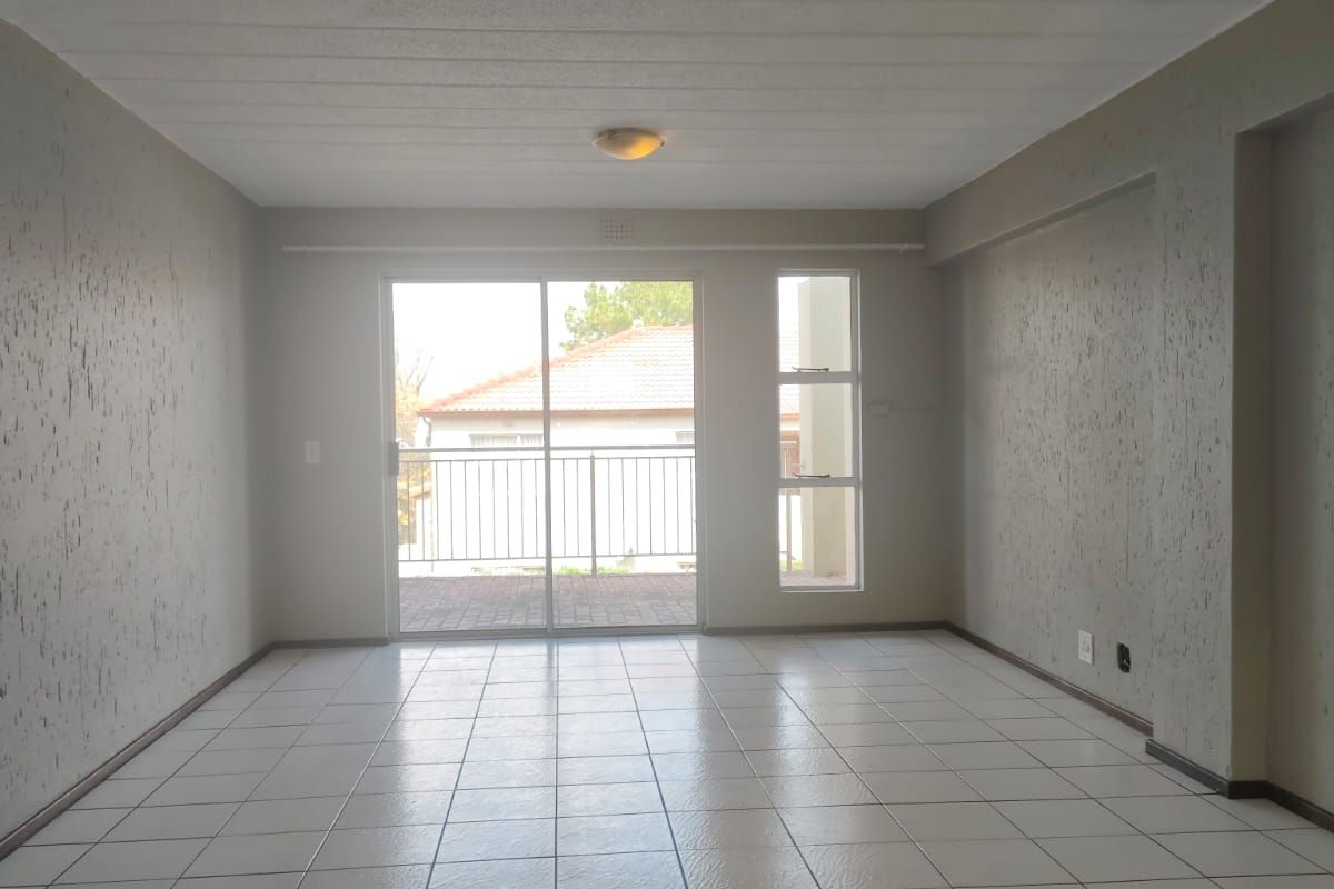 An empty, open-plan living area featuring neutral tiled flooring, textured walls, and a sliding glass door providing access to an outdoor balcony.