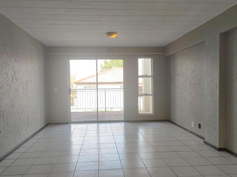 An empty, open-plan living area featuring neutral tiled flooring, textured walls, and a sliding glass door providing access to an outdoor balcony.