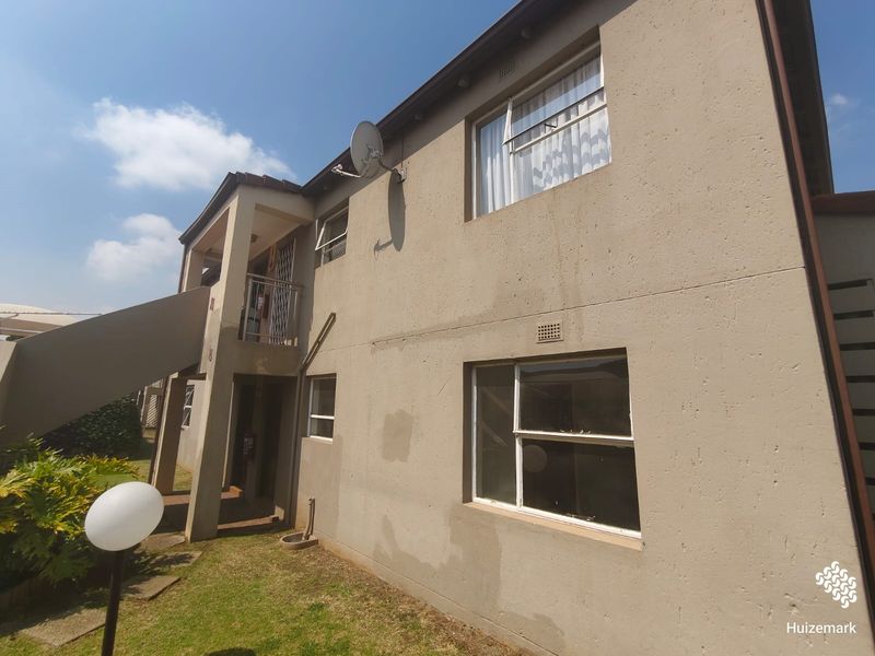 Rear view of a two-story townhouse featuring a plastered facade, external staircase, balcony, and sliding windows.