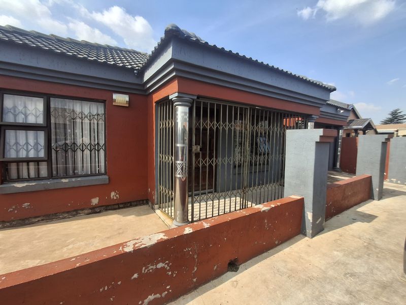 Front exterior view of the house featuring a concrete boundary wall, security gates, and tiled roof, showing signs of weathered paint and surface wear.