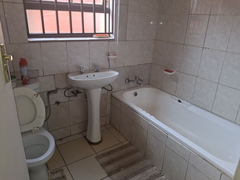 A functional bathroom featuring a pedestal basin, bathtub, and toilet with neutral wall and floor tiling, requiring cosmetic updates to improve its overall condition.
