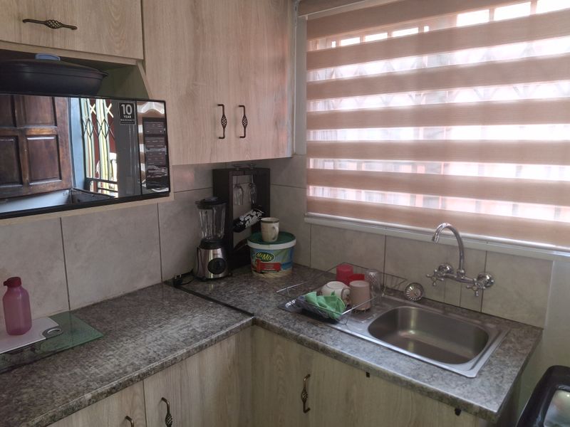 A functional kitchen featuring light wood-tone cabinetry, durable laminate countertops, a stainless steel sink, and a tiled backsplash with natural light from the window.
