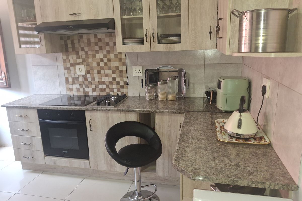 A functional kitchen featuring light wood-grain cabinetry, granite-look laminate countertops, a built-in oven with hob, and a decorative mosaic tiled backsplash.