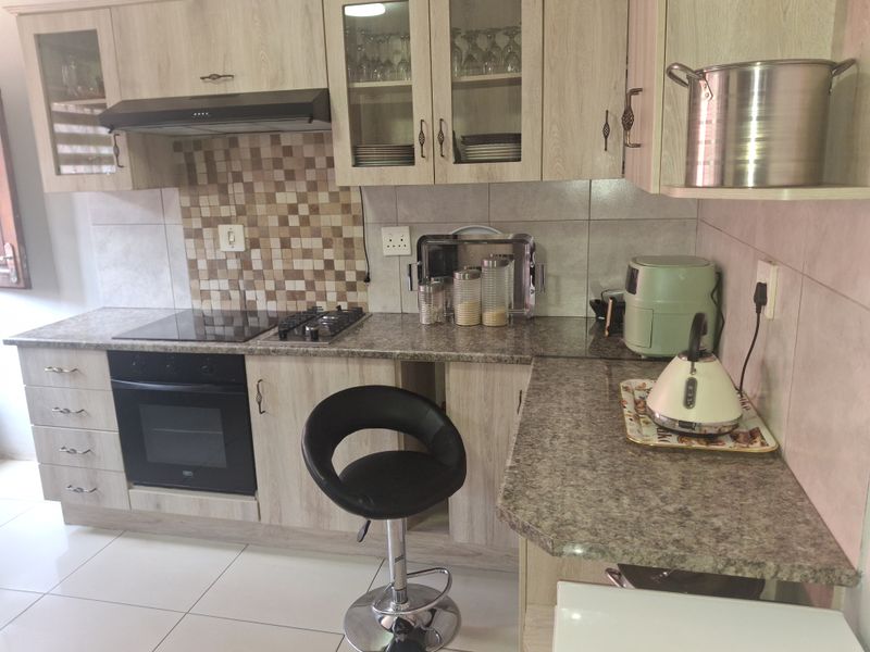 A functional kitchen featuring light wood-grain cabinetry, granite-look laminate countertops, a built-in oven with hob, and a decorative mosaic tiled backsplash.